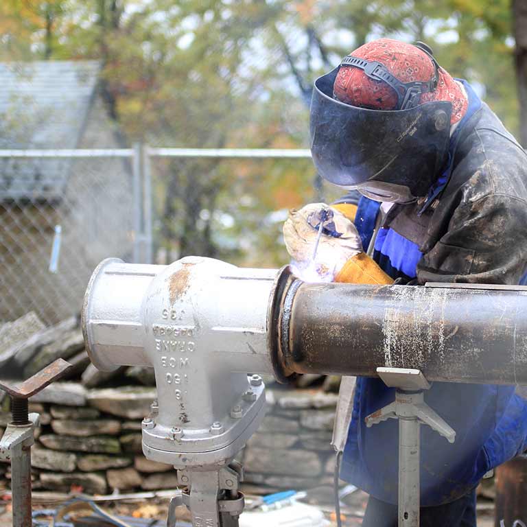 A worker repairs a metal pipe with a welding gun. 