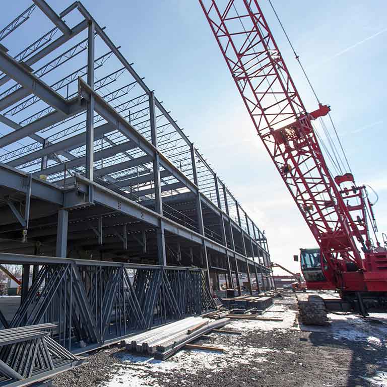 A construction crane sites next to a metal building frame. 